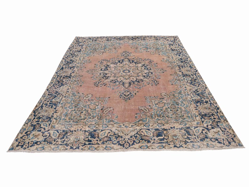 May include: A large, rectangular rug with an intricate floral pattern. The rug features a central field in a muted rose color, surrounded by a border of navy blue and cream. The design includes detailed floral and geometric motifs.