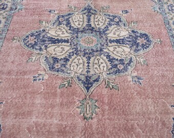 May include: A vintage rug with a distressed, faded appearance. The rug features a central medallion design in navy blue, cream, and teal, set against a dusty rose background. The intricate pattern includes floral and geometric elements.