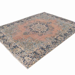 May include: A large, rectangular area rug with an intricate floral pattern. The rug features a central medallion design in shades of pink and blue, surrounded by a dark blue border with floral motifs. The rug's design is detailed and ornate.