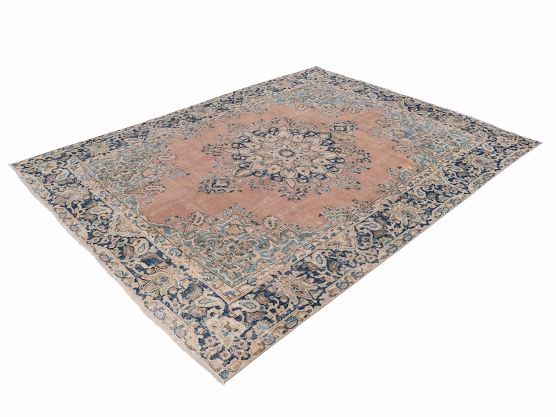 May include: A large, rectangular area rug with an intricate floral pattern. The rug features a central medallion design in shades of pink and blue, surrounded by a dark blue border with floral motifs. The rug's design is detailed and ornate.