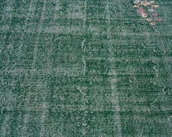 May include: A close-up of a green rug with a woven texture. The rug has a faded appearance, giving it a vintage look.