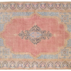 May include: A vintage rug with a pink background and intricate floral patterns in shades of blue, beige, and black. The rug has a central medallion and a border with repeating motifs.