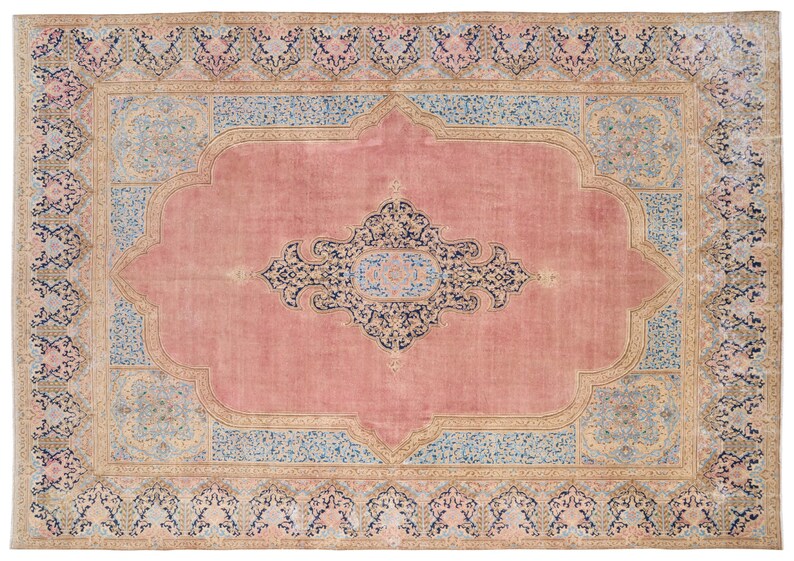 May include: A vintage rug with a pink background and intricate floral patterns in shades of blue, beige, and black. The rug has a central medallion and a border with repeating motifs.