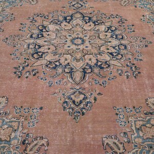 May include: A large, rectangular rug with an intricate floral pattern. The rug features a faded, distressed look with a color palette of muted rose, navy blue, and cream. The central design is a large medallion.