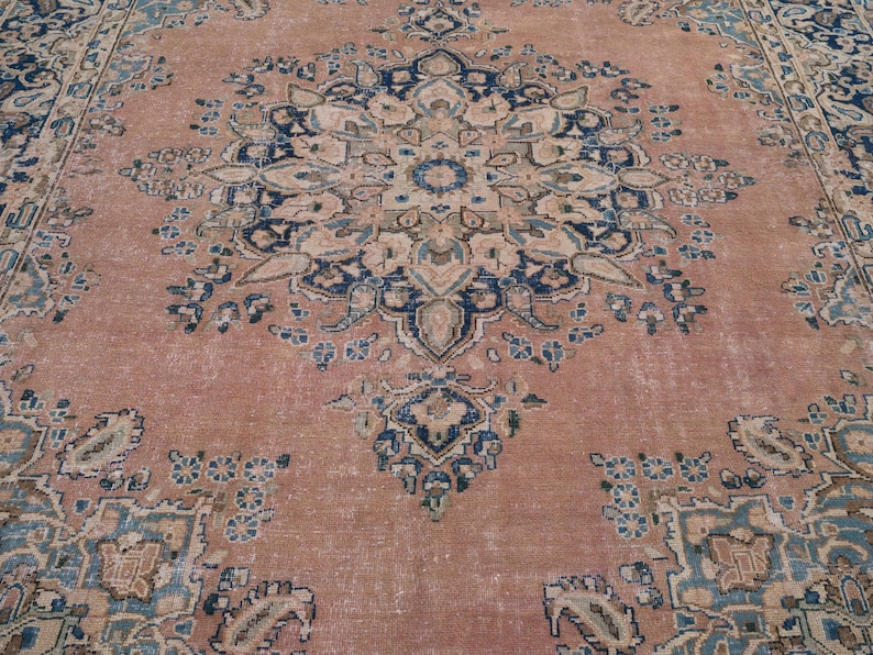May include: A large, rectangular rug with an intricate floral pattern. The rug features a faded, distressed look with a color palette of muted rose, navy blue, and cream. The central design is a large medallion.