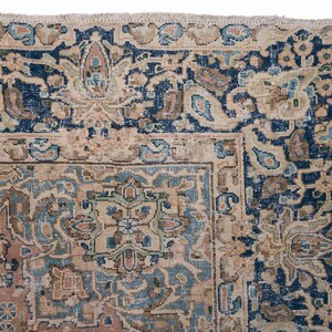 May include: Close-up of a section of a vintage rug with an intricate floral design. The rug features a color palette of navy blue, beige, and muted pink. The border is a deep navy blue with floral patterns, and the central design has a beige background with blue and pink accents.
