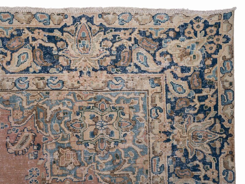 May include: Close-up of a section of a vintage rug with an intricate floral design. The rug features a color palette of navy blue, beige, and muted pink. The border is a deep navy blue with floral patterns, and the central design has a beige background with blue and pink accents.