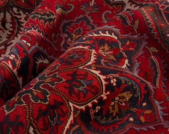May include: Close-up of a richly patterned red rug with intricate floral and geometric designs. The rug features a deep red background with accents of navy blue, beige, and touches of gold. The detailed patterns create a textured appearance.
