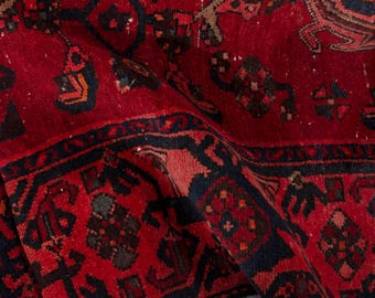 May include: Close-up of a red and navy blue patterned rug. The rug features a detailed geometric design with a central field of red and intricate borders. The rug's texture is visible, with slight variations in color.
