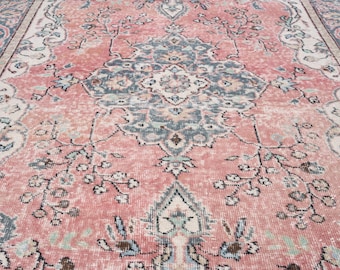 May include: A distressed, vintage-style rug with a faded, floral pattern. The rug features a central medallion design in shades of dusty rose, teal, and cream. Delicate floral and vine motifs are scattered across the field, creating a soft, aged appearance.
