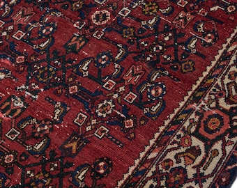 May include: A red rug with a traditional Persian design. The rug has a dark blue border with a cream and red pattern. The center of the rug is a deep red with a floral and geometric design.