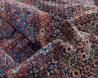 Könnte beinhalten: Nahaufnahme eines gefalteten Teppichs mit traditionellem persischen Design. Der Teppich weist eine reichhaltige Farbpalette aus tiefen Blautönen, Rottönen und Creme auf, mit komplizierten floralen und geometrischen Mustern. Die Textur und die Falten des Teppichs sind sichtbar.