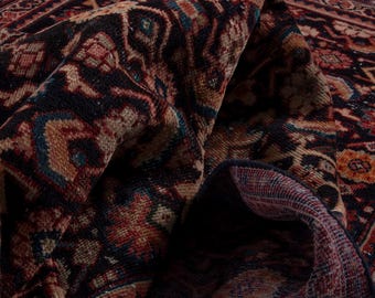 May include: Close-up of a folded, vintage rug with intricate patterns. The rug features a rich color palette of deep reds, navy blues, and warm browns. The design includes geometric and floral motifs, showcasing a traditional style.