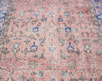 May include: A vintage rug with a distressed, faded appearance. The rug features a central field of muted pink with an intricate floral pattern in blue, green, and brown. A blue border frames the edges, adding contrast to the overall design.