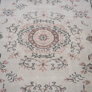 May include: A beige rug with a repeating pattern of pink and black floral designs. The rug has a central medallion with a pink and black floral design.