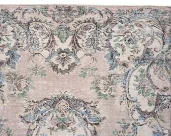 May include: Close-up of a section of a vintage rug with an ornate floral pattern. The rug features a faded color palette of pink, cream, blue, and green. The design includes stylized flowers and scrolling vines, creating a classic, aged aesthetic.