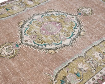 May include: A distressed, vintage-style rug in shades of dusty rose, sage green, and teal. The rug features an ornate, central medallion design with floral and geometric patterns. The overall aesthetic is faded and worn, suggesting an antique or well-loved piece.