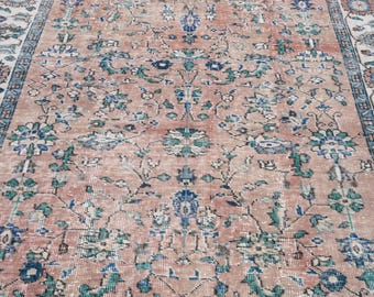 May include: A vintage rug with a distressed, faded appearance. The rug features a central field of muted peach with a floral pattern in shades of blue and green. The border has a similar design with a cream background.