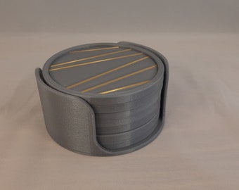 May include: A set of six gray coasters with a gold geometric pattern on the top coaster. The coasters are stacked in a holder.