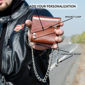 May include: A brown leather wallet with a chain attached. The wallet has a magnetic clasp and a carabiner mount. The wallet is personalized with the letters "ABC".