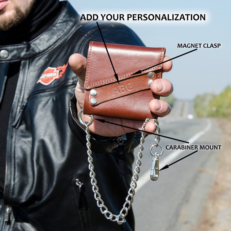 May include: A brown leather wallet with a chain attached. The wallet has a magnetic clasp and a carabiner mount. The wallet is personalized with the letters "ABC".