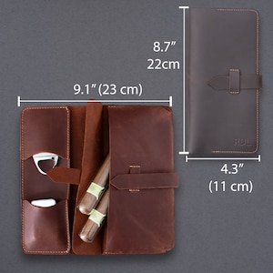 May include: A brown leather cigar case with a strap closure, featuring internal pockets for a metal cutter and lighter, and space for two cigars. The case measures 9.1 inches by 8.7 inches when open, and 8.7 inches by 4.3 inches when closed with RDL embossed.