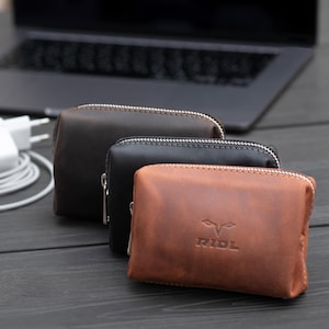 May include: Three leather zippered pouches in brown, black, and tan. The tan pouch has the word "RIDL" embossed on the front.