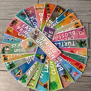 May include: A collection of colorful, illustrated bookmarks arranged in a circular pattern. Each bookmark features a unique design with text, including words like "Spring Unicorn," "Easter," and "Lucky." The illustrations include a unicorn, a bee, and a turtle.