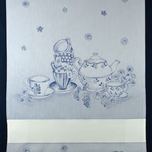 May include: A light blue tea towel with a floral and teacup design. The towel features a teapot, teacups, and daisies in a detailed blue illustration. The bottom of the towel has the text "Gitti Tessiana 1841 Made in Italy."