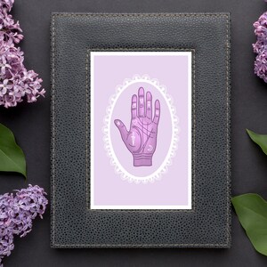 May include: A black picture frame with a white mount and a purple background. The image inside the frame is a hand with lines and symbols, representing a palmistry reading.
