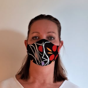 May include: A woman wearing a black face mask with a colorful abstract design featuring red, yellow, and white accents.