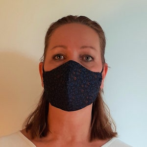 May include: A person wearing a dark blue face mask with a small white and orange floral pattern.
