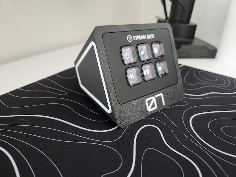 May include: Black Stream Deck with six illuminated buttons and the Stream Deck logo. The device is on a black and white topographic patterned mousepad. The number "07" is printed on the front.