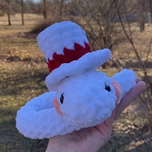 Puede incluir: Juguete de peluche blanco con un sombrero de copa rojo y blanco. El juguete tiene un cuerpo redondo y una carita pequeña con ojos negros y mejillas rosadas.