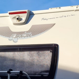 K&ouml;nnte beinhalten: Ein wei&szlig;er Wohnwagen mit einem grauen und silbernen "Signature"-Logo und dem Text "Making memories one road trip at a time..." auf der R&uuml;ckseite. Der Wohnwagen hat ein Heckfenster mit einem grauen Netzgitter und eine R&uuml;ckfahrkamera.