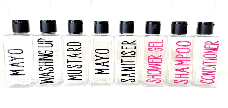 May include: Eight clear plastic bottles with black pump tops and labels. The labels have black and pink text. The labels read "MAYO", "WASHING UP", "MUSTARD", "MAYO", "SANITISER", "SHOWER GEL", "SHAMPOO", and "CONDITIONER".