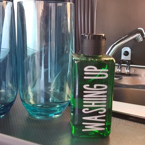 May include: Two clear blue glass tumblers and a green bottle with a white label that says "Washing Up" on a gray countertop.