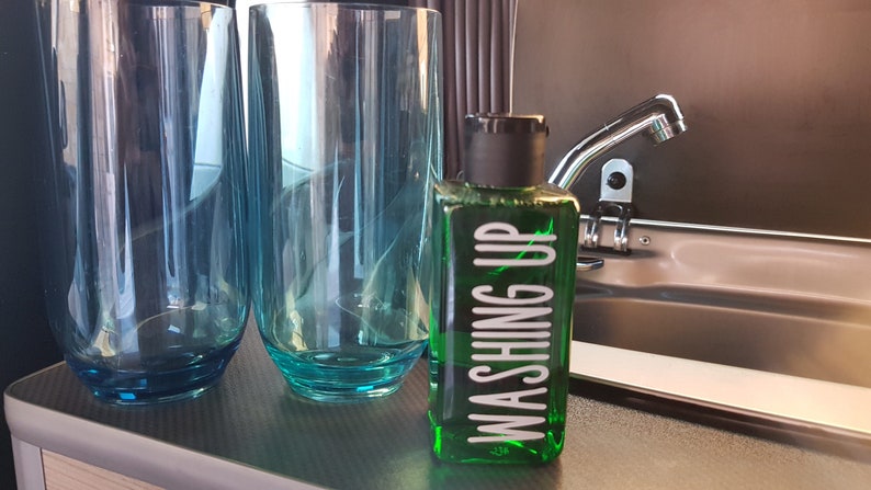 May include: Two clear blue glass tumblers and a green bottle with a white label that says "Washing Up" on a gray countertop.