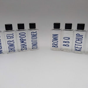 May include: Eight clear plastic bottles with black lids and blue labels. The labels read "Washing Up", "Shower Gel", "Shampoo", "Conditioner", "Brown", "BBQ", "Ketchup", and "Mayo".