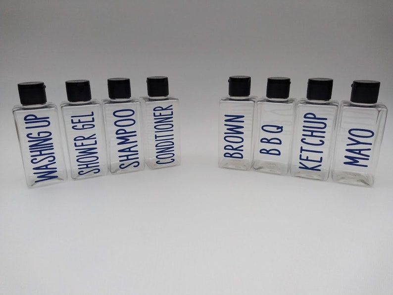 May include: Eight clear plastic bottles with black lids and blue labels. The labels read "Washing Up", "Shower Gel", "Shampoo", "Conditioner", "Brown", "BBQ", "Ketchup", and "Mayo".