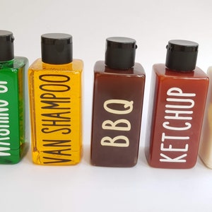 May include: Five clear plastic bottles with black caps and white labels. The labels read "Washing Up", "Van Shampoo", "BBQ", "Ketchup", and "Mayo".