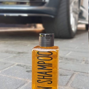 May include: A clear bottle of yellow shampoo with a black cap and the text "VAN SHAMPOO" printed on the bottle.