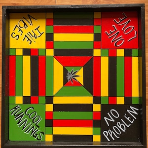 Peut inclure: Un plateau de jeu en bois avec un cadre noir et un motif de grille coloré. Les cases ont des phrases différentes écrites dessus, notamment "Cool Runnings", "No Problem", "One Love" et "Irie Vibes".