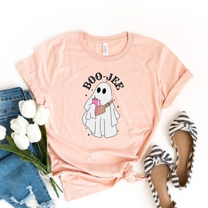 May include: A heather peach colored t-shirt with a ghost holding a pink drink and the text "BOO-JEE" printed on the front.
