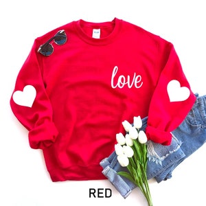 May include: Red sweatshirt with the word "love" printed on the front and white hearts on the sleeves.