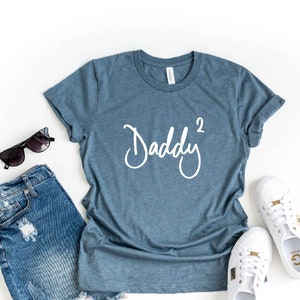 May include: Heather slate blue t-shirt with the text "Daddy 2" in white script font.