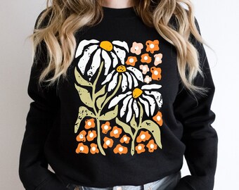 May include: Black sweatshirt with a white and orange floral print. The print features large daisies and smaller flowers.
