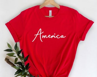 May include: Red t-shirt with the word "America" written in white cursive lettering.