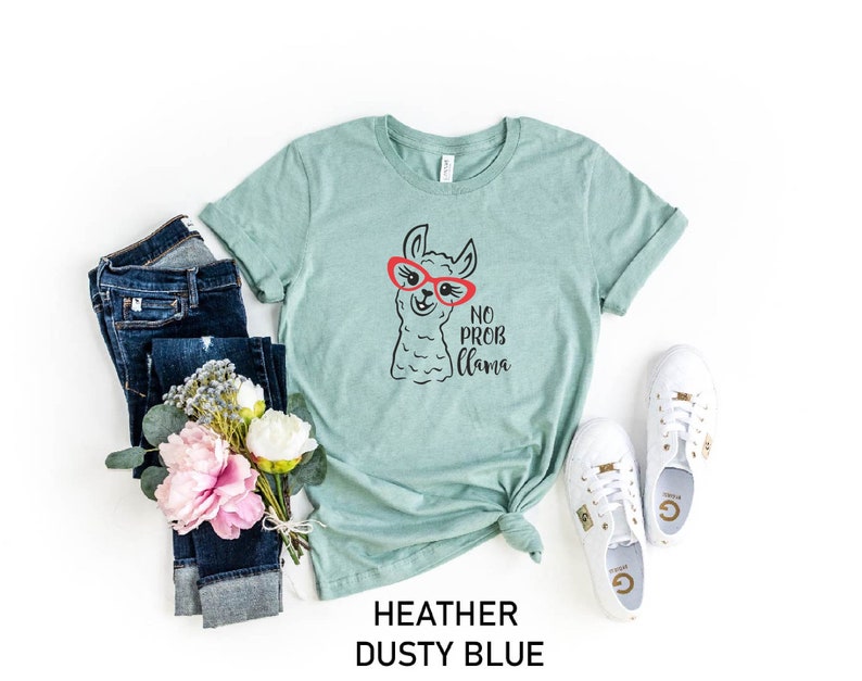 May include: A heather dusty blue t-shirt with a black and white illustration of a llama wearing red sunglasses. The text "No Prob Llama" is printed below the llama.