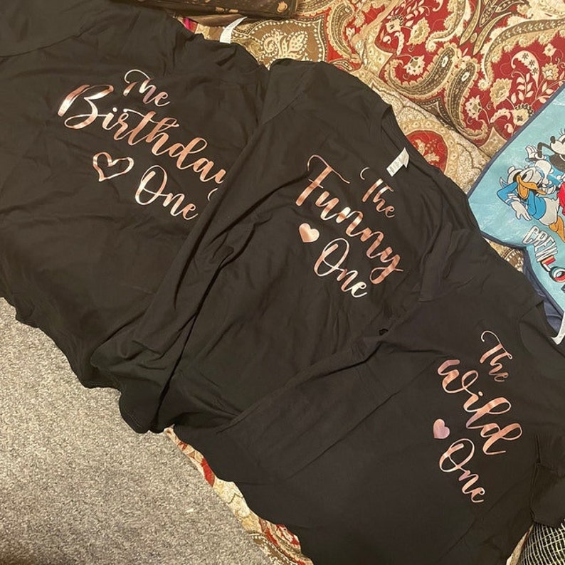 May include: Three black t-shirts with rose gold foil lettering. The shirts say "The Birthday One", "The Funny One", and "The Wild One".